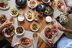 several people are sitting at a table with food in bowls and plates on the table