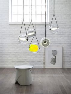 a room with white brick walls and wooden flooring, hanging glass orbs over the table