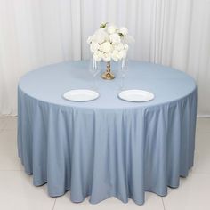 two white flowers are sitting on top of a blue round table with plates and wine glasses