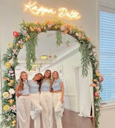 three women standing in front of a mirror with flowers on the wall and happy birthday sign above them