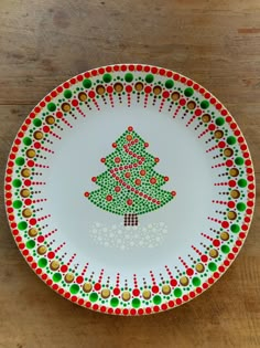 a plate with a christmas tree painted on the side and dots around it, sitting on a wooden table