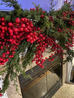 red berries and greenery are hanging over the fireplace