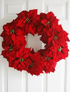 a wreath with red poinsettias hanging on the front door for holiday decor