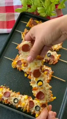 someone is picking up some pizza on a stick with olives and pepperoni in the middle