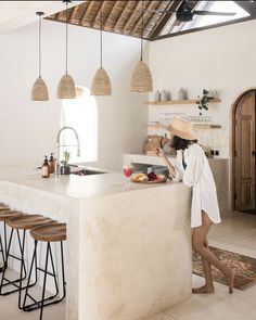 a woman standing at the counter in a kitchen next to stools and an island