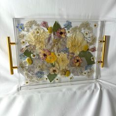 a glass frame with flowers in it on a white sheet covered tablecloth and gold handles