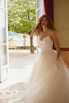 a woman in a wedding dress is standing near an open door and looking at the camera