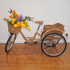 a bicycle with flowers in the basket is parked on a wooden floor next to a wall