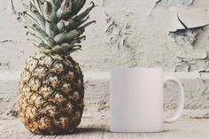 a pineapple sitting next to a white coffee mug on a wooden table in front of a painted wall