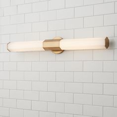 a bathroom light that is on the side of a white brick wall in front of a tiled wall