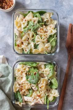 two plastic containers filled with pasta salad next to a wooden spoon and bowl of seasoning