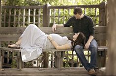 a pregnant woman laying on top of a wooden bench next to a man