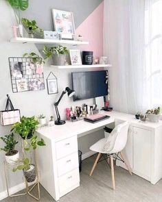 a white desk topped with a computer monitor next to a window filled with potted plants