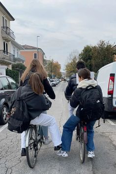 two people riding on the back of a bike down a street next to parked cars