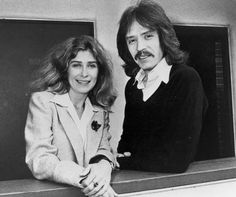 two people standing next to each other in front of a black and white photo with long hair