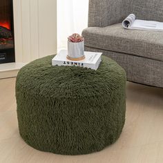 a small round ottoman with a book on it in front of a fire place and couch