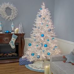 a white christmas tree with blue and silver ornaments in a living room next to a fireplace