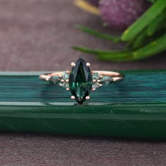 a green tourmaline and diamond ring sitting on top of a piece of wood