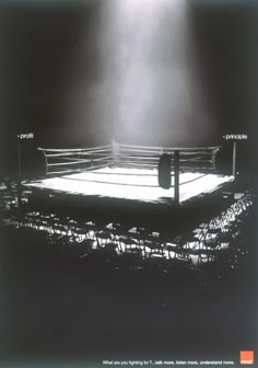 an empty boxing ring in the middle of a dark room with light coming from behind it