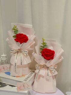 two red roses are placed on top of each other in paper wrapped boxes with ribbons