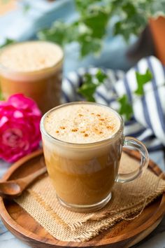 two cups of coffee sitting on top of a wooden tray next to pink flowers and greenery