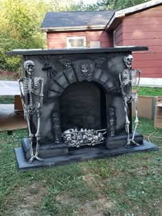 an outdoor fireplace with skeleton decorations on the front and sides, sitting in grass next to a red house