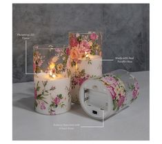 two white candles with pink roses on them are next to an electrical outlet and plug