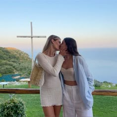 two women standing next to each other in front of a cross on top of a hill