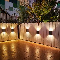 some lights that are on the side of a fence and in front of a plant