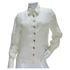 Elevate your wardrobe with the Chanel 90s White Linen Button Down Shirt – a classic and timeless piece that exudes sophistication. Crafted from lightweight ivory linen, this collared button-down shirt features silver-tone buttons adorned with Chanel logos, creating a subtle yet luxurious touch. The shirt's classic collar and breast pockets add a traditional charm, while the silver-tone buttons down the center and at the wrists showcase the iconic Chanel branding. The combination of crisp white l Elegant Linen Tops With Buttons, Single-breasted Linen Button-up Top, Elegant Linen Tops With Button Closure, Classic Cream Linen Shirt, Elegant Linen Office Top, Elegant Linen Tops For Office, Elegant Linen Blouse With Button Closure, Classic Cream Button-up Shirt, Classic Linen Shirt For Office