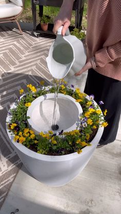 a person is pouring water into a flower pot with flowers in the bottom and around it