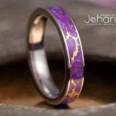 a purple and gold wedding ring sitting on top of a wooden table next to a piece of wood