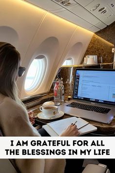 a woman is sitting in an airplane with her laptop and notepad on the desk