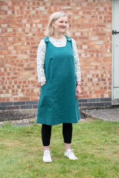 a woman standing in front of a brick building wearing a green dress and white shoes