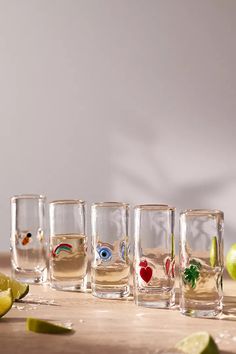 four shot glasses filled with different types of drinks on a wooden table next to limes and an apple