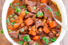 a bowl of beef stew with carrots and parsley in it on a cutting board