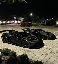 two black sports cars parked next to each other in a parking lot at night time