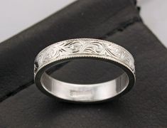 a wedding ring with an intricate design on it's side, sitting on a black cloth