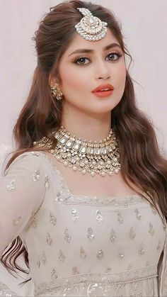 a woman with long hair wearing a white dress and gold jewelry on her head, posing for the camera