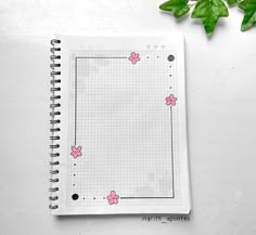 an open notebook with pink butterflies on it next to some green leaves and a plant