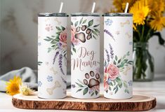 three personalized tumbles with dog paw prints and flowers on them, sitting on a wooden board