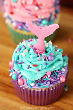 two cupcakes with blue and pink frosting on them, one has a mermaid tail