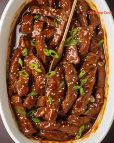 beef with sesame seeds and sauce in a white bowl on a black tablecloth, with chopsticks