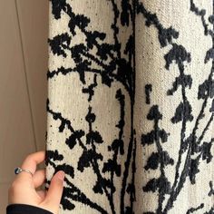 a person is holding onto the curtain with their hand and it has black flowers on it