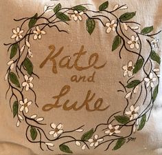 a pillow with the words kate and luke written in gold on it, surrounded by white flowers