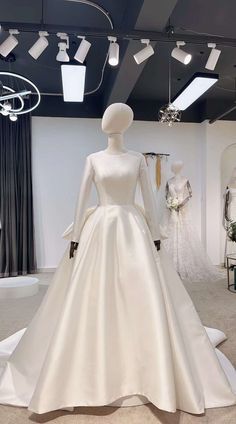 a white wedding dress on display in a room with mannequins and dresses