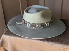 The Bandit is a stand out hat that captures the feeling of the American West. . The base of the hatband is distressed leather that is then layered with imprinted brown leather, bolo sliders and lots of nailspots. It is finished with this colorful feather combo. The brim of the LID custom hat body is 4" in diameter and the crown is 4.5". This is a stiff hat. Available in Putty or Pecan All hats are made to order. Allow up to 4 weeks for your hat to ship. Distressed Brown Brimmed Hat, Distressed Brown Hat For Country Events, Distressed Brown Hat For Rodeo, Brown Leather Felt Hat For Rodeo, Western Distressed Brown Hat, Western Style Brown Leather Felt Hat, Custom Brown Hat Bands For Festival, Distressed Brown Western Hat, Brimmed Hats With Leather Sweatband For Country Events