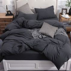 an unmade bed with dark gray linens and pillows