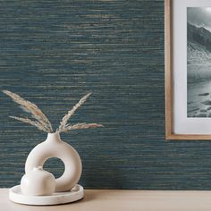 a white vase sitting on top of a wooden table next to a painting and framed photograph