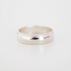 a white gold wedding ring with beaded edges on a plain surface, ready to be worn